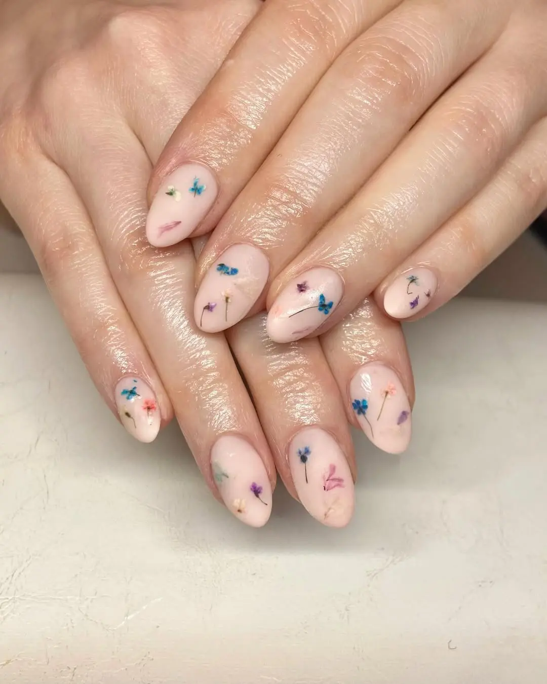 Echte oder gemalte Mini-Blumen, die wie gepresst aussehen, sorgen für einen romantischen Look. Besonders beliebt auf milchigen Bases ("Milky Nails"). Neta und Lena setzen diese feinen Details mit höchster Präzision um.