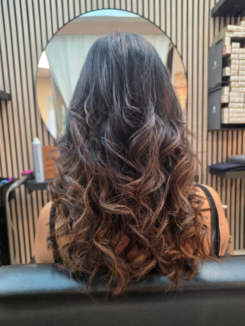 Lange braune Locken mit hellen Balayage-Spitzen von hinten im Beautycenter by Neta St. Gallen